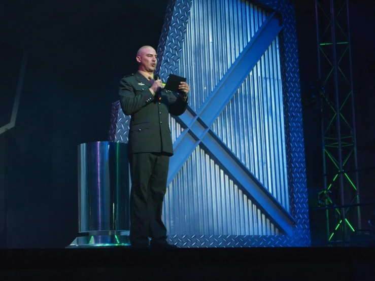 a man in a black suit and blue tie holding up a camera on stage