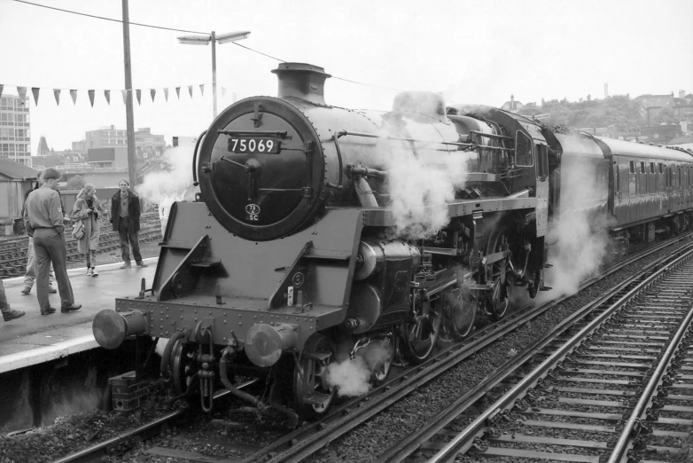 old fashioned steam train passing a platform as it is smoking