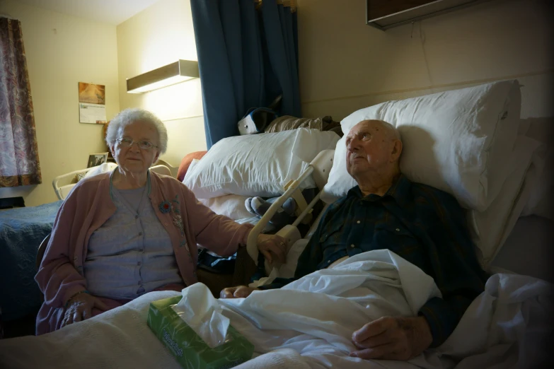 an elderly couple sitting on the couch and laying in bed