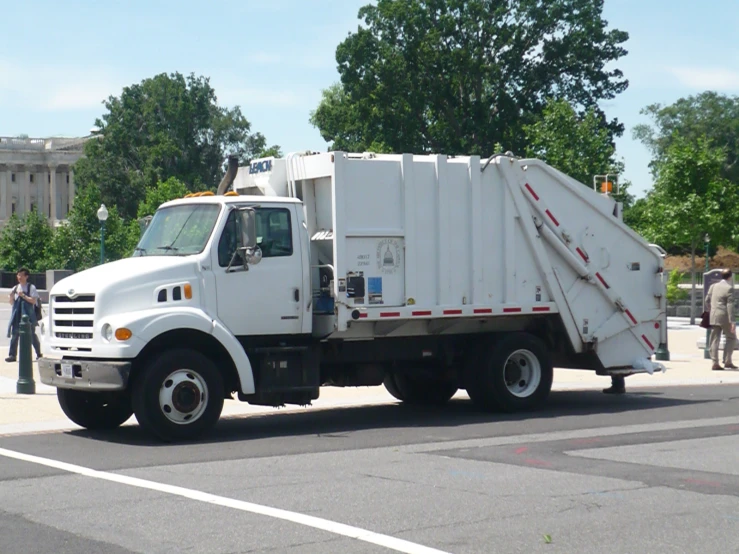 white trash truck driving down the street with others in the distance