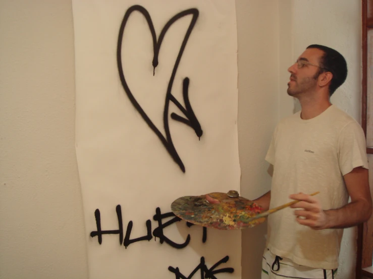 a man holds a palette next to a graffiti - covered wall