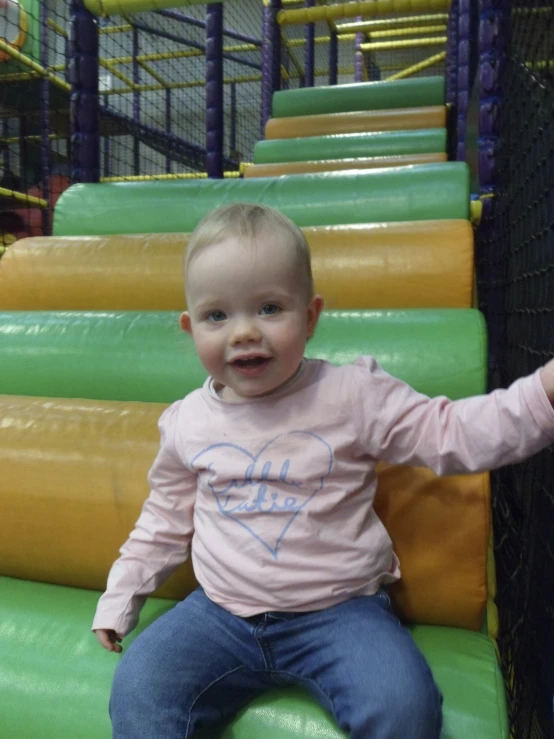 the young child smiles as he sits on a colorful slide