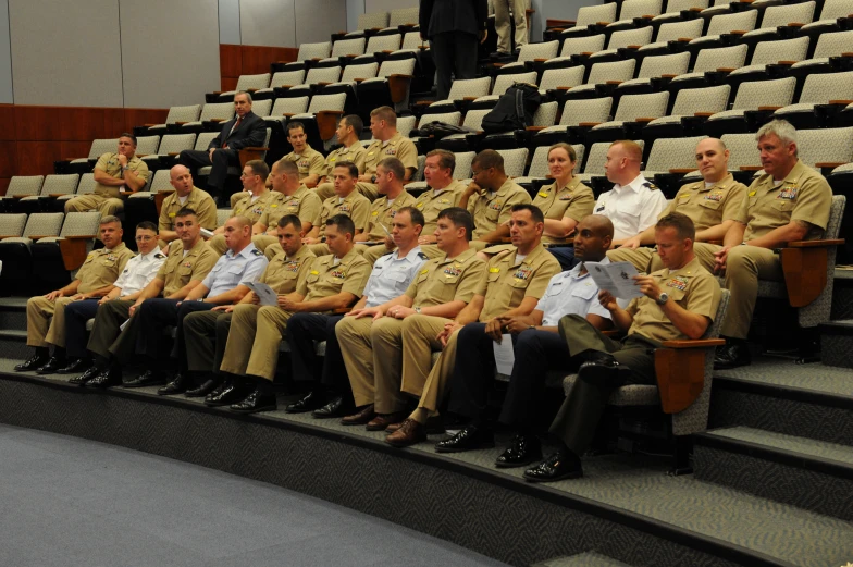 a large group of people wearing uniforms and sitting down in chairs