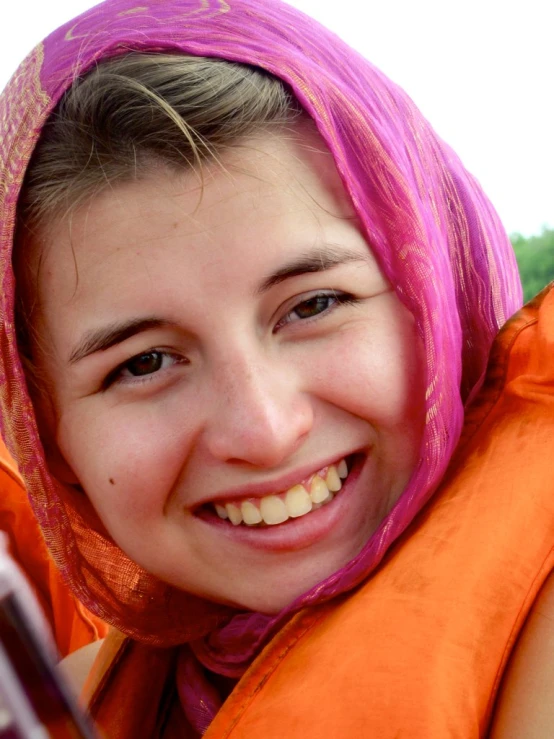 a girl with pink hair and orange vest smiling for a picture