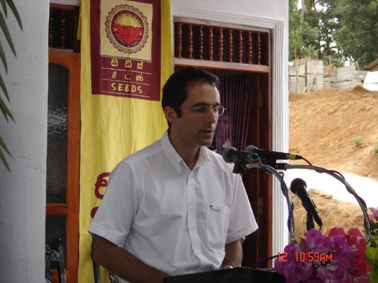 man speaking into microphone in front of outdoor area