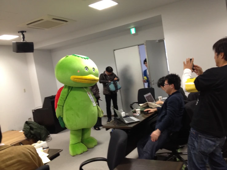 some people are standing in a room and one is holding up a stuffed toy and another person has on his lap