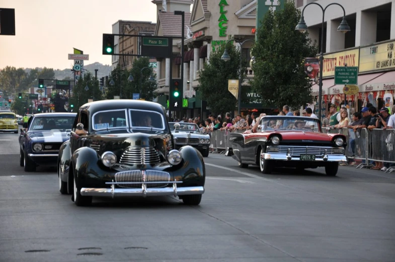 old cars are driving through the street with other classic vehicles
