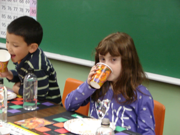 two children are sitting at a table drinking beverages