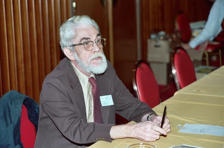 an older man sitting at a table with a pen