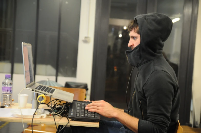 a man in a black hooded sweatshirt typing on a laptop