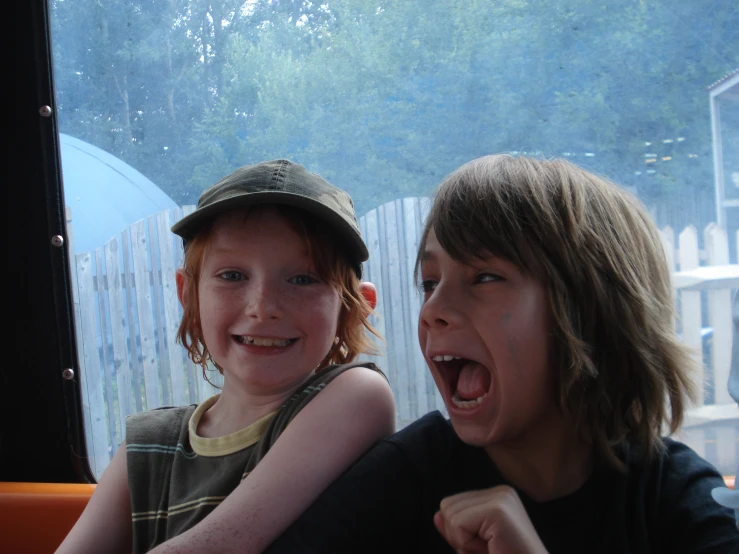 two children sitting at a table and a boy holding a banana