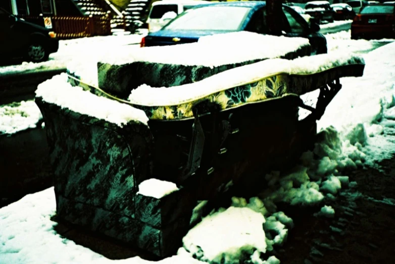 an old bench with snow on it and cars in the background