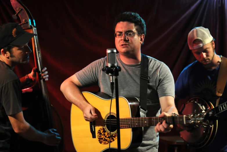 a man wearing glasses is playing a guitar and singing into a microphone