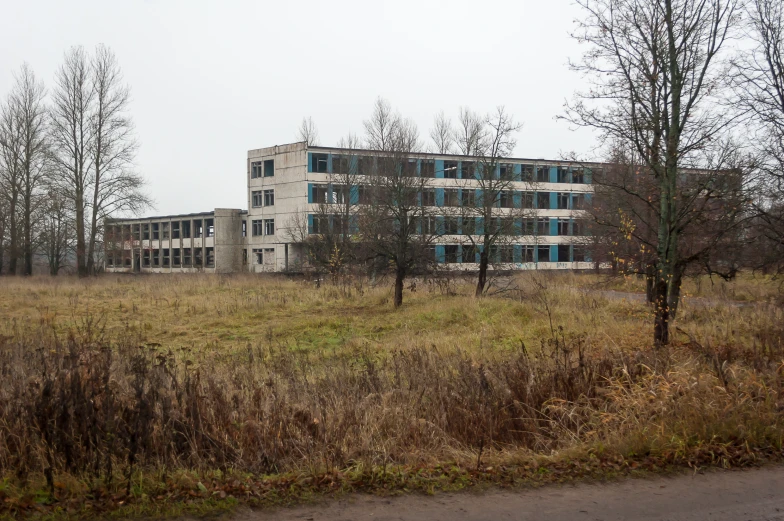 an abandoned building with lots of windows and overgrown grass in front