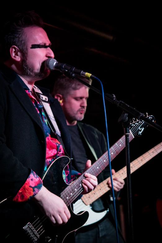 two men singing into microphones and playing guitar on stage