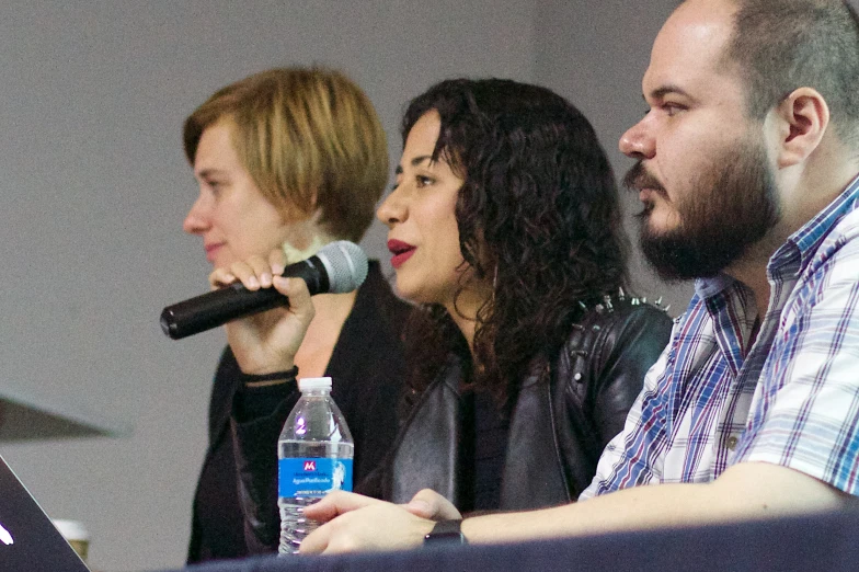 three people sitting on a stage, one speaking