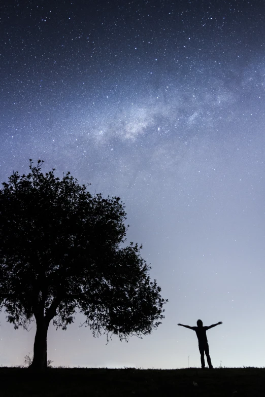a lone person standing under the stars while holding his arms out and looking up