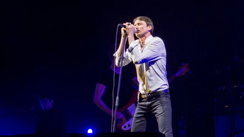 a man in white shirt and tie singing into microphone