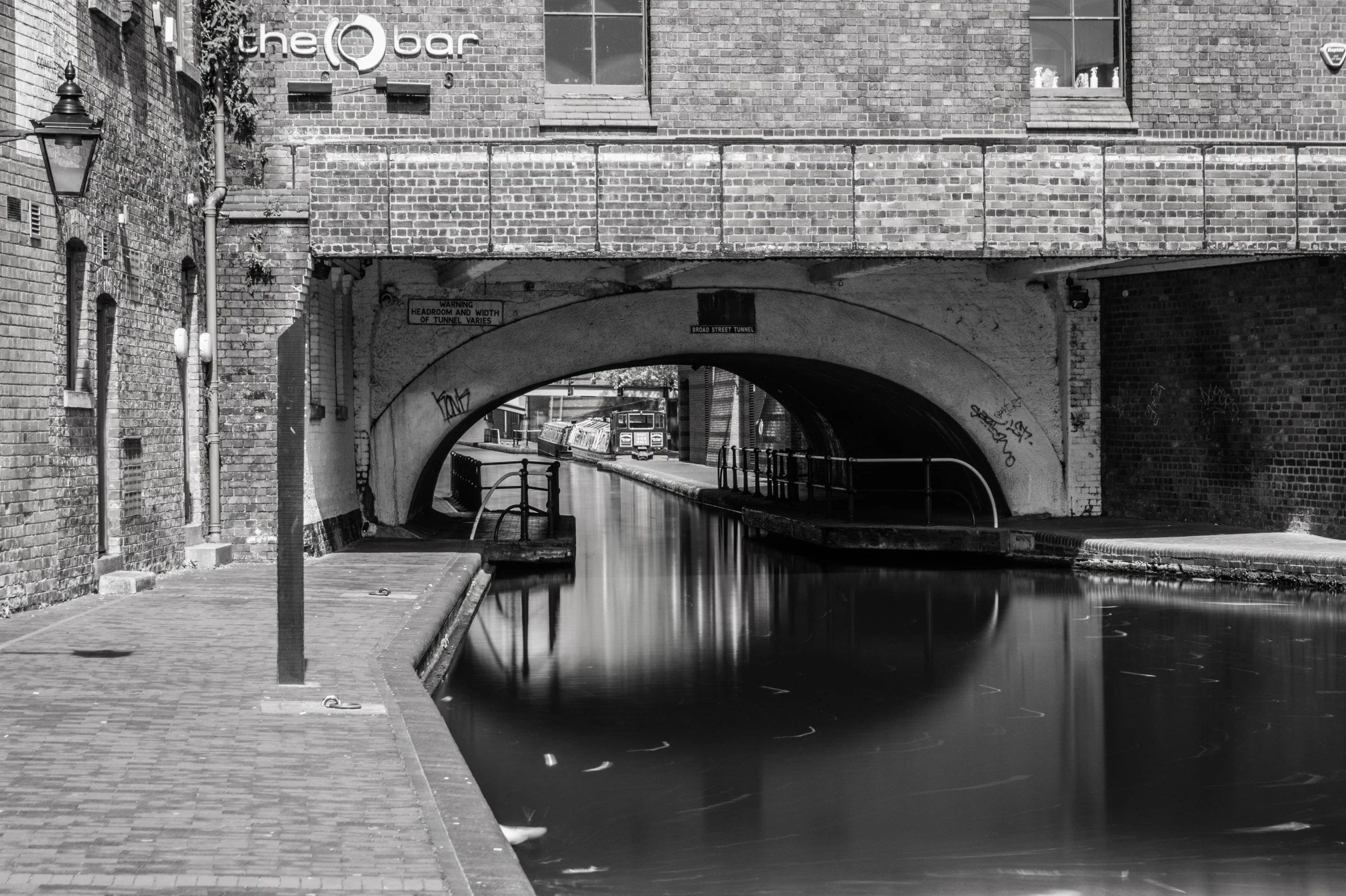 a black and white po with brick walls, waterway and an arch overpass