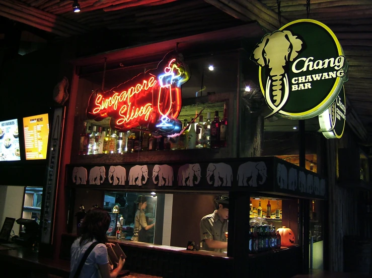 a neon sign above a restaurant with people walking in front