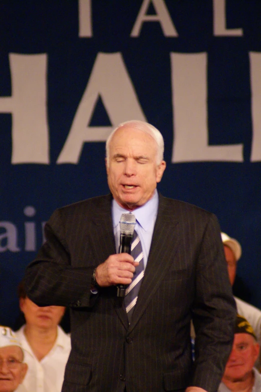 an older man in a suit and tie holding a microphone