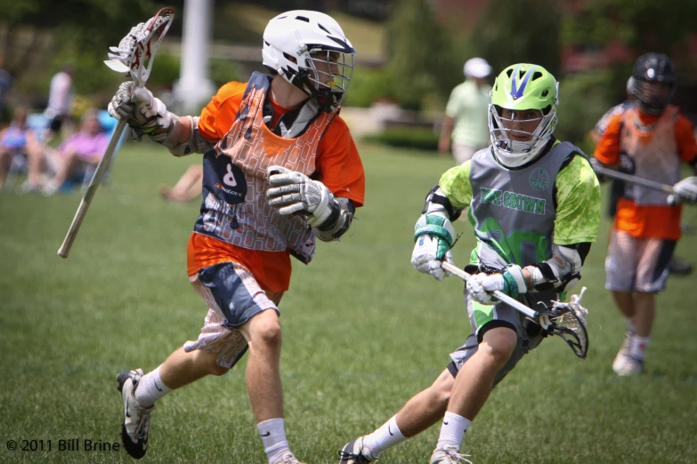 two young men are playing lacrosse in a grassy field