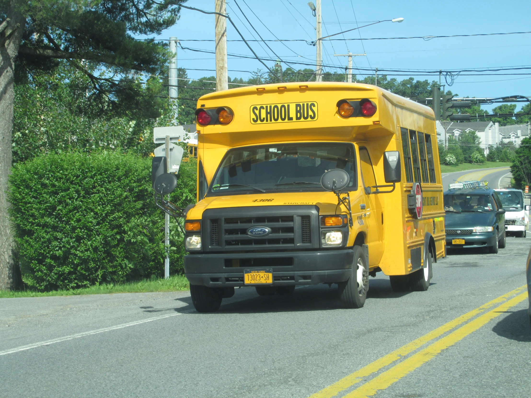 yellow school bus driving down the road near the woods