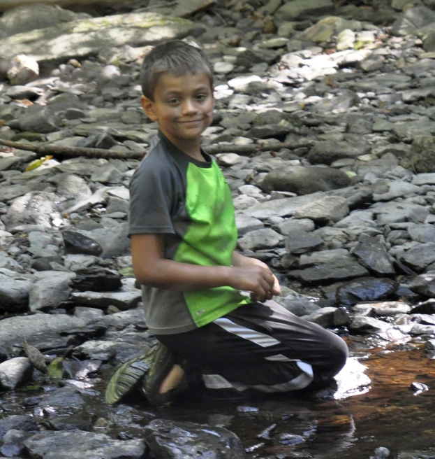 a boy is sitting on the edge of a rocky stream