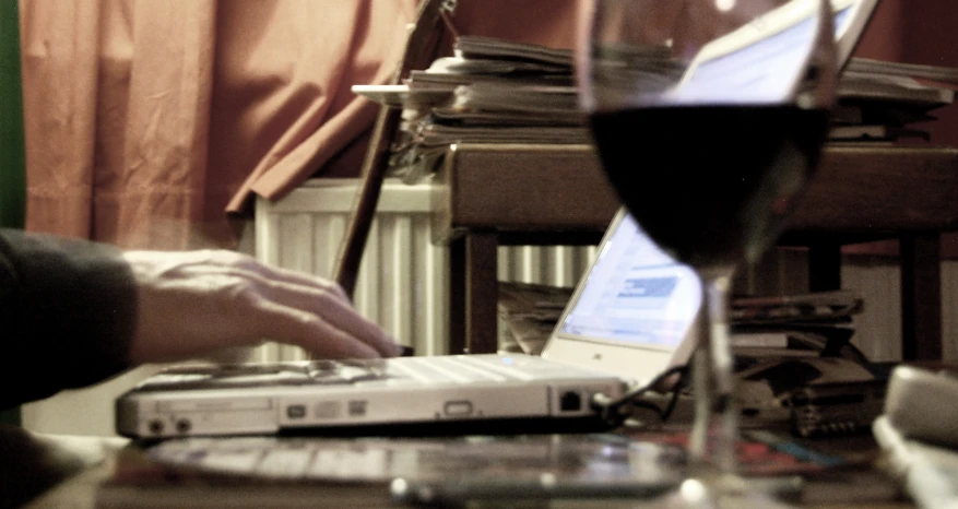 a persons hands are on their laptop near the wine glass