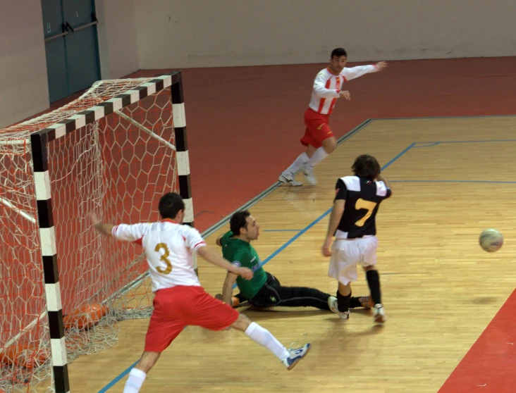 three young men playing soccer on a indoor court