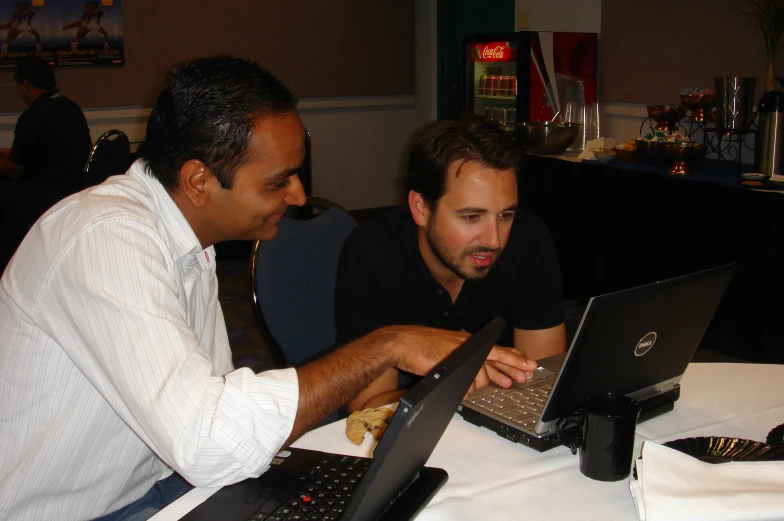 two men are using their laptops at a table