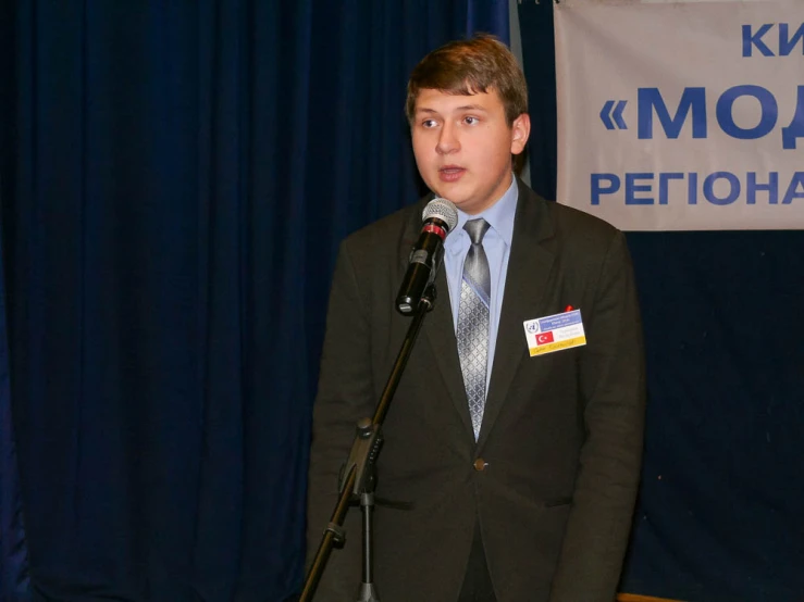 a man with a suit and tie speaks in front of a microphone