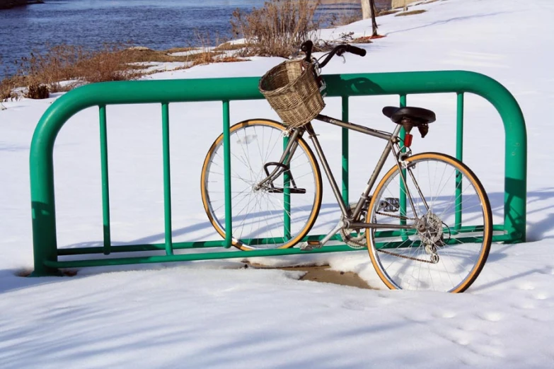 bicycle  to green iron railing with snow and river