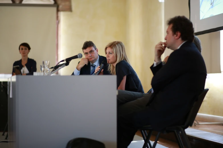 two men and a woman at a podium speaking into microphones