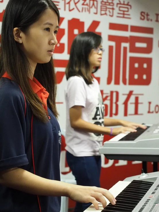 an asian girl with long brown hair playing the piano while another girl looks on