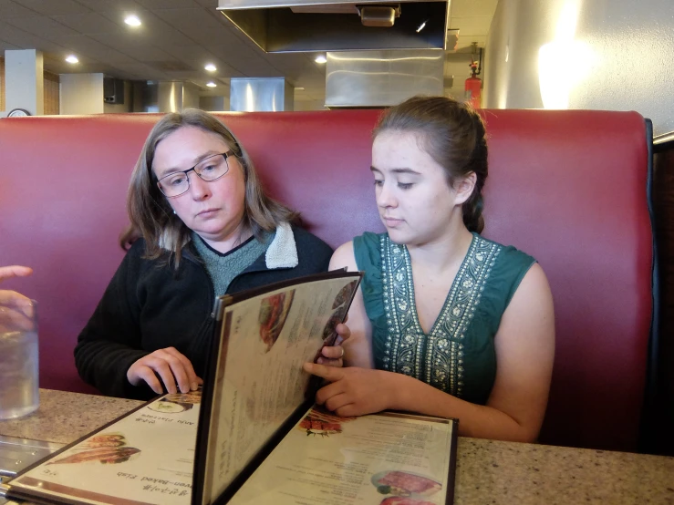 two women sitting at a booth while one reads