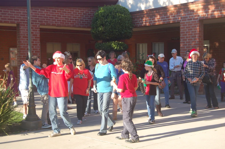 a group of people in red shirts outside a building with people standing near by