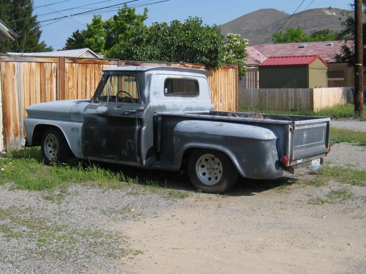 an old pickup truck is parked by a fence