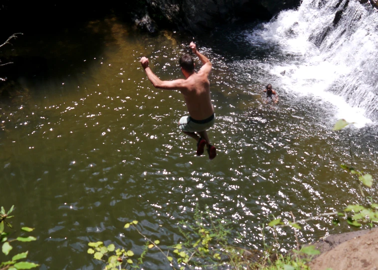 a man is jumping into the river in front of a waterfall
