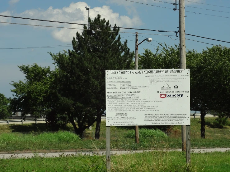 a white sign on a pole in front of trees