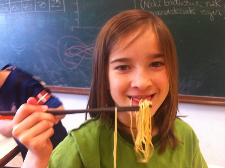 a girl smiles while eating a noodle dish