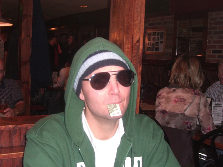 a man in green hoodie and sunglasses holding a drink