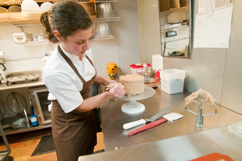 a woman in white shirt and brown apron decorating cake