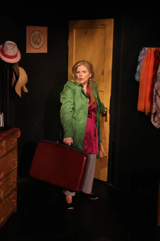 a woman in green coat holding suitcase standing next to wooden wardrobe