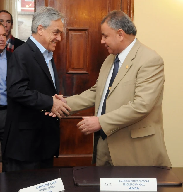 two men shaking hands in front of a wooden desk