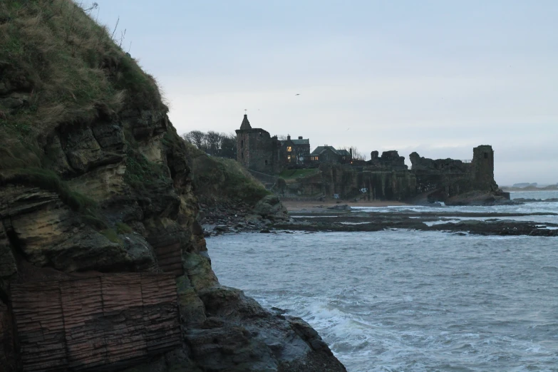 a cliff that is in the middle of the ocean with a castle in the distance