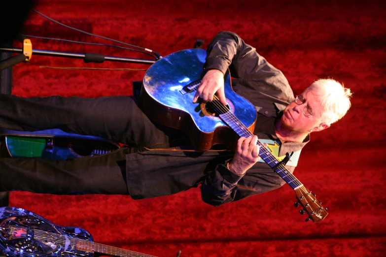 a man playing an acoustic guitar in front of a red curtain