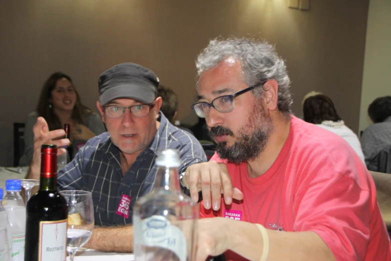 two men are sitting down at a table looking at a bottle