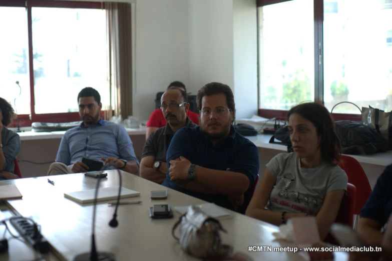 several people sitting around tables with pens and laptops