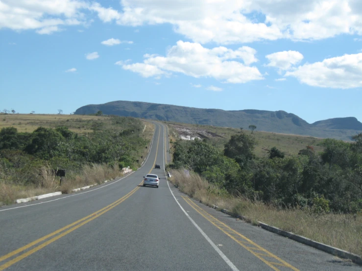 the car is driving down the highway, just past a hill